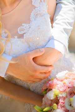 Photo of a wedding couple in the summer. Bride and groom hugging, hands, rings, wedding bouquet close-up and copy space.