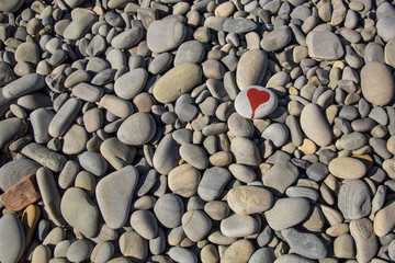 stone heart painted with a red paint marker on the pebble as a gift for Saint Valentine day on the pebble background.