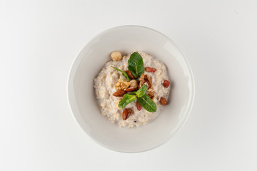 Oatmeal porridge with milk, almond, hazelnuts, honey and apple, decorated with mint leaves for a healthy breakfast, isolated on white