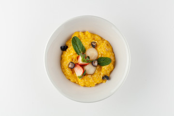 Yellow corn porridge with milk, berries, mint for a healthy nutritious breakfast, isolated in white