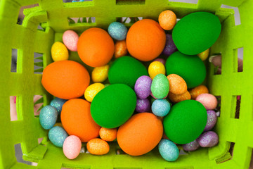 Eggs of birds of different colors and sizes lie in a green basket. Artificial products imitating poultry eggs. Easter colorful eggs of different sizes in a basket