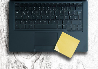 top view of yellow sticky note on laptop keyboard against white wooden table