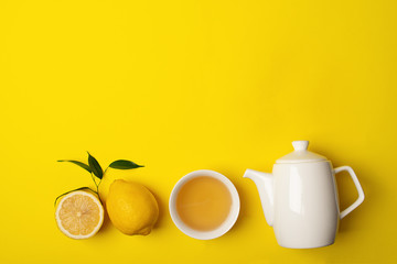 Fresh lemon tea or detox drink in a white cup and a teapot on a bright yellow background. Healthy eating concept.