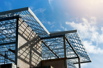 Roof frame of under construction house..Metal roof frame structure of a two story house without  roof tiles under sunny cloud blue sky,low angle view.