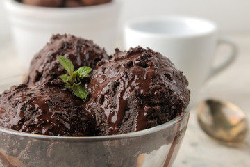 Chocolate ice cream with liquid chocolate and cinnamon sticks on a light concrete background.