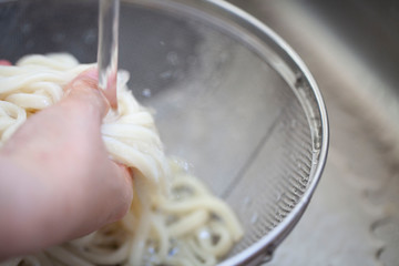 ザルの中で水でうどんを洗う