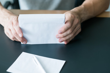 Invitation letter. Cropped shot of man sitting at desk with stack of white envelopes and blank sheet of paper. Copy space.