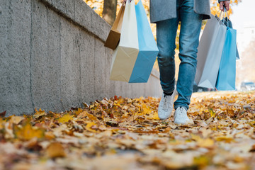 Autumn shopping. Cropped shot of man walking with packages along fall sidewalk covered with yellow...