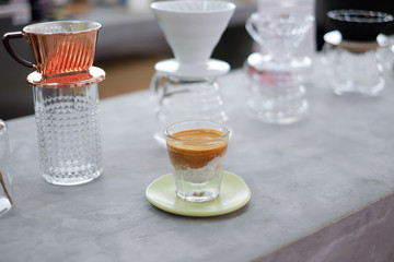 A glass of hot coffee latte with beautiful gradient place on wood coaster, yellow background with selective focus.