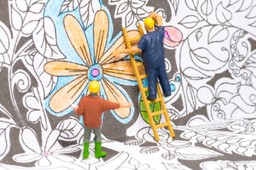 Macro shot on miniature figures as painters working on colouring details on a wallpaper