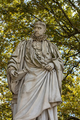 Statue of Michel de Montaigne in public garden along Place des Quinconces, Bordeaux France, with a canopy of green trees.