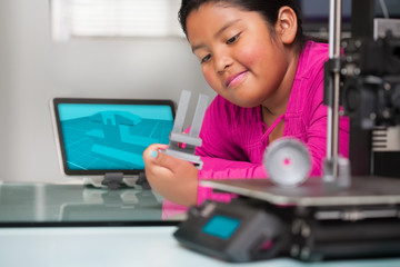 Pre teen girl examines her 3d printed part and looks like she is thinking about making revisions to the design.