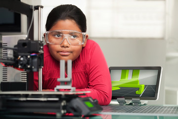 A cute little girl in studio setting thinks of ideas for her 3d printed design that is printing in...