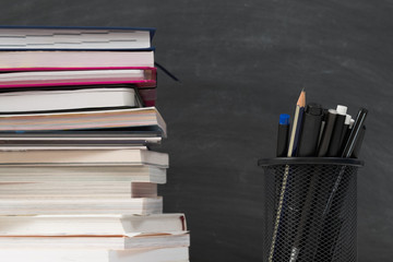 Education concept. Closeup of book stack, stationery over empty black chalkboard. Copy space.