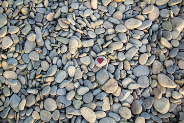 stone heart painted with a red paint marker on the pebble as a gift for Saint Valentine day on the pebble background.