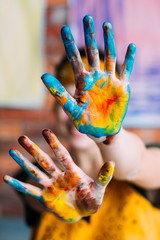 Creative hobby. Female artist showing hands dirty with blue and yellow paint. Blur background.