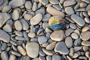 Bright sun painted on pebble. Pebbles and sea background.
