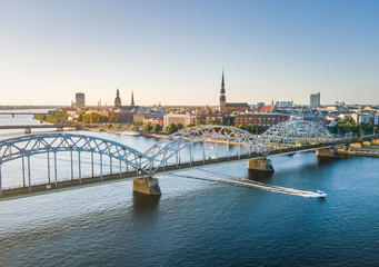 Fototapeta premium Panoramic view over Riga city at sunset. Iconic railroad bridge and old town panorama. Picturesque scenery of historical architecture. National library of Latvia. 