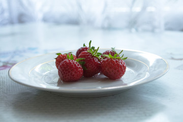 Fresh home-grown strawberries with green peduncles served on white plate