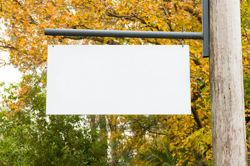 Advertising empty white blank board hanging on a wooden pole on the right, with nature forest in the background. Copy space available for text
