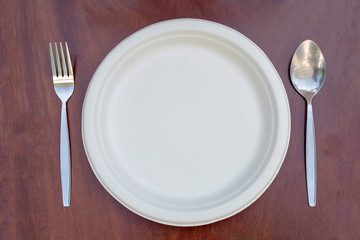 Paper plates can be resized on a wooden floor with a spoon and stainless steel fork placed.