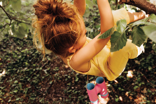 Happy child wearing yellow romper, swinging on a tree in the summertime in the park. Adorable blond little girl playing at nature background. tip view image of cheerful kid having fun in the forest.