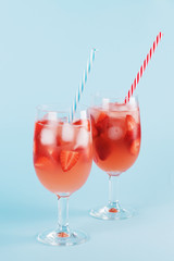 Fresh strawberry summer cocktail and ice cubes. Two glasses with strawberry, ice and wine - strawberry sangria on a pastel blue backgound, minimalism