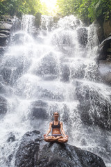 Obraz premium Woman practices yoga near waterfall in Bali, Indonesia
