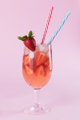 Fresh strawberry summer cocktail and ice cubes. Glass with strawberry, ice and wine - strawberry sangria on a pastel pink backgound, minimalism