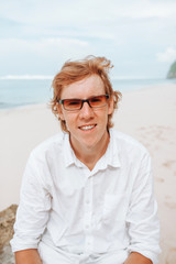 Portrait of a red-haired man in white clothes on a white beach in sunglasses