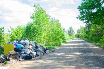 Illegal dump near the country sand road in the country on sunny day. Trash pollution in the nature....
