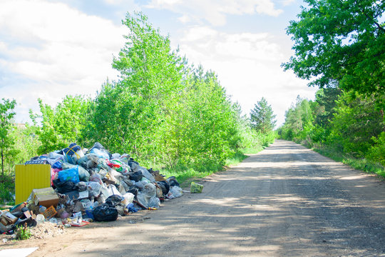 Illegal dump near the country sand road in the country on sunny day. Trash pollution in the nature. Dirty dump near forest woods
