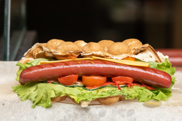 Delicious bubble waffle with fried egg and sausage slices on wooden board, closeup