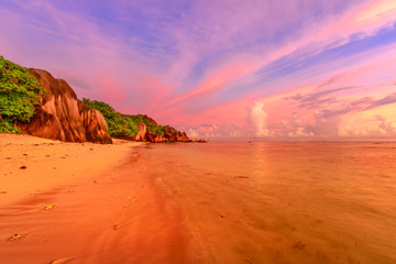 Seychelles, La Digue, Anse Source d'Argent at twilight. Landscape of colorful clouds in the sky on rock stone of granite boulder. Calm and tranquil sea on the horizon.