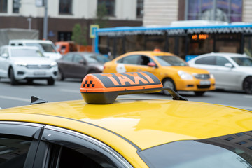 Fototapeta na wymiar Yellow cab with taxi sign on the roof parked on the city street waiting for passengers to pick up.The taxi is parked on the street of the big city.Focus on the yellow lamp icon