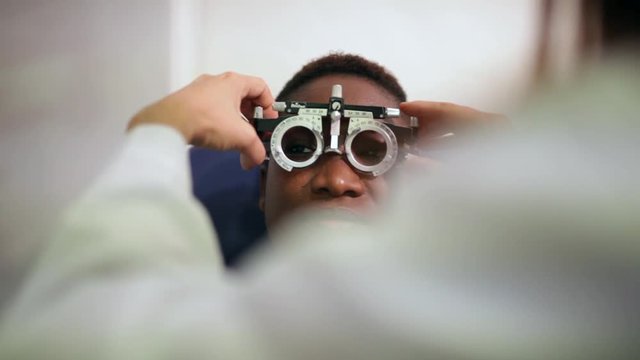 afro woman checking her eyesight to become glasses with optometry tools