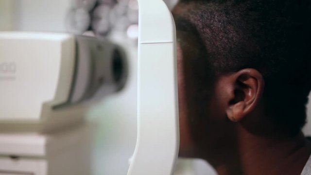 side view of an afro woman in an optometry cabinet correcting her eyesight	with a ophthalmometer
