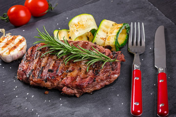 Juicy medium rare beef steak slices on ceramic board with herbs spices and salt.