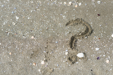 question mark wriiten on a sandy beach. Concept of faq, travel tips and travel destinations