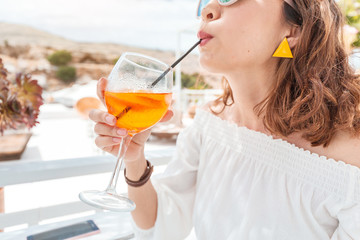 Happy asian woman enjoying aperol spritz cocktail in a greek cafe. Beverage and refreshment concept