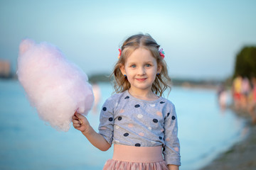 happy little girl holding cotton candy in her hand resting in nature on the river Bank standing on the beach