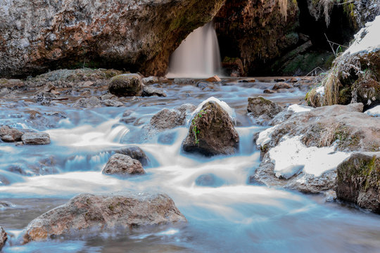 Cold mountain river flows between stones with snow and ice, selective focus, waterfall in the background, long exposure, Karachay-Cherkess Republic