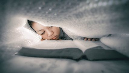 Focus at face. Boy reading bible under the covers at night and fell asleep.
