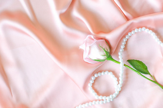 Gently pink rose with a pearl necklace on satin fabric.