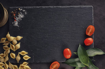 Pasta shells on black stone. Tomatoes and bay leaves with allspice and sea salt.
