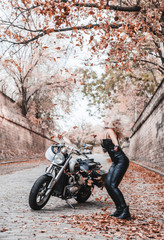 Beautiful biker woman posing with autumn leaves on the road.