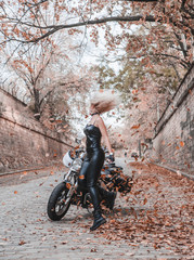 Beautiful biker woman posing with autumn leaves on the road.