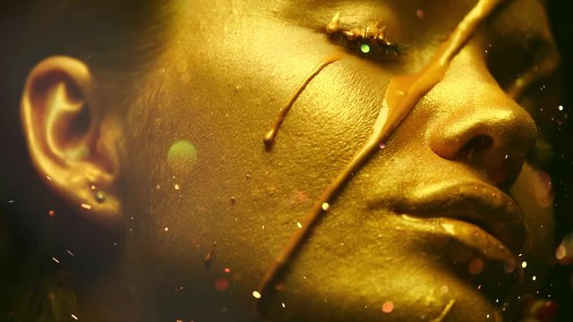 Sexy beauty woman with golden metallic skin. Gold paint smudges drips from the face and sexy lips. Creative makeup. Slow motion 4K UHD video footage. 3840X2160
