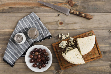 Roquefort cheese slice; olives with salt and pepper shaker on wooden table