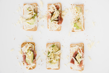 Toast bread with grated cheese; ham and avocado slice on white backdrop